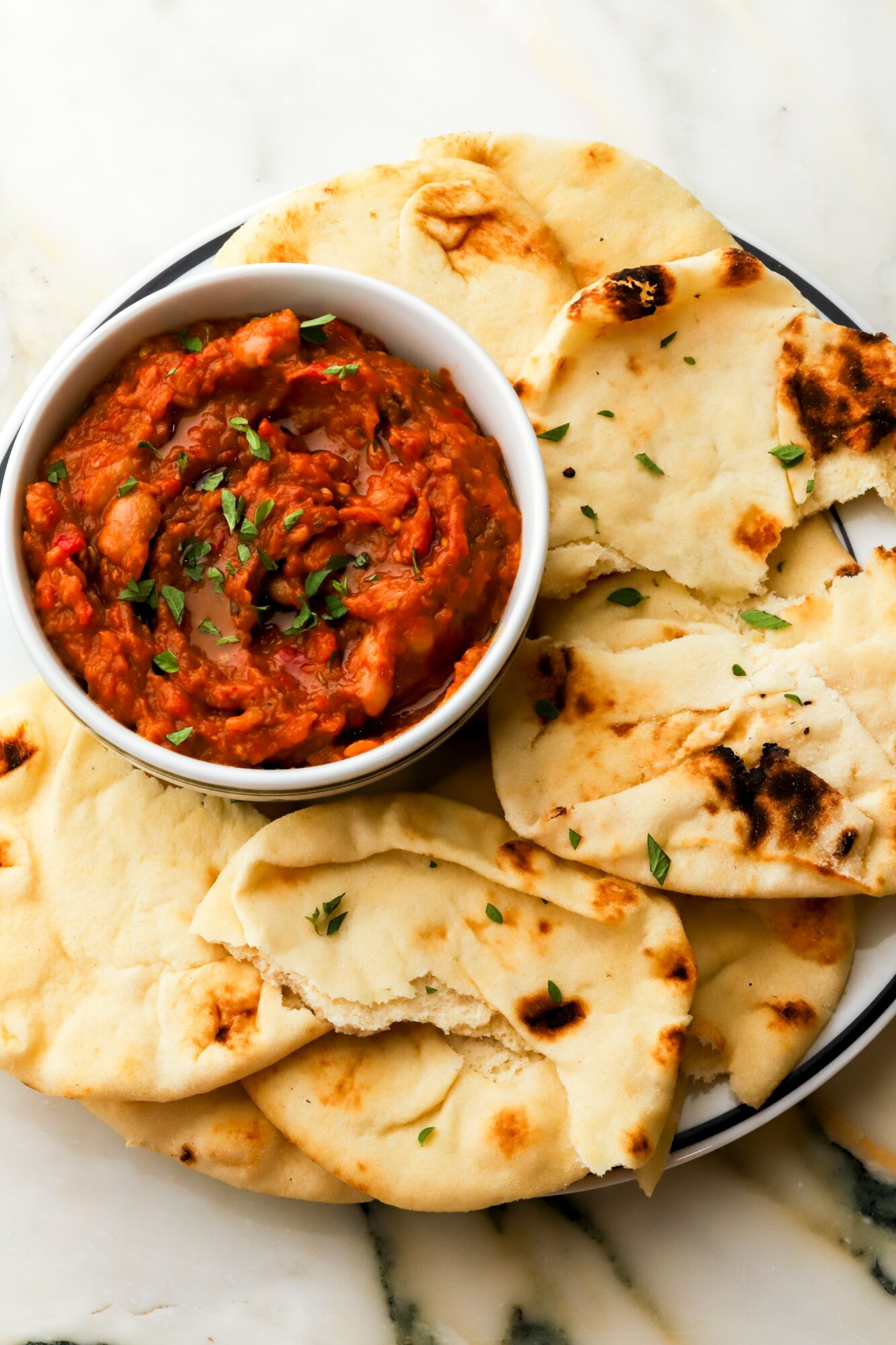 Bowl of spicy tomato-based curry with naan bread on a white surface.