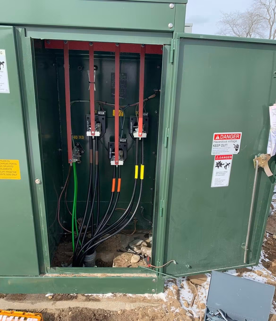 Open electrical cabinet with wires and components inside, outdoors, with trees in the background.