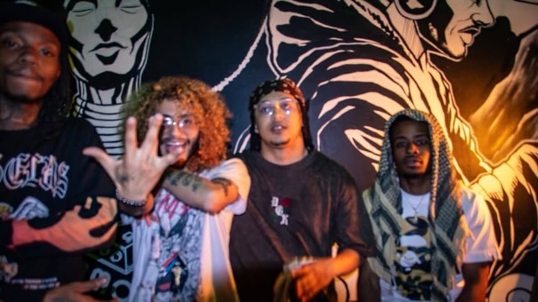 Four people standing in front of a mural with black and white portraits, smiling and posing for the camera.