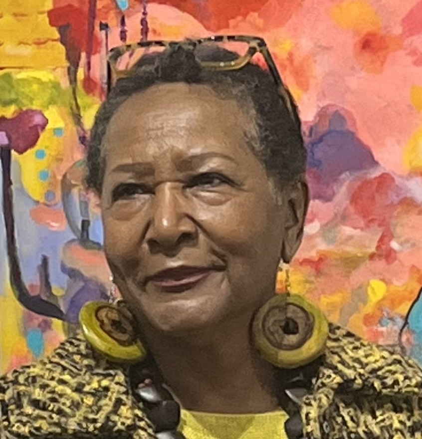 Portrait of a woman with short hair, wearing large circular earrings and a patterned top, against a colorful abstract background.