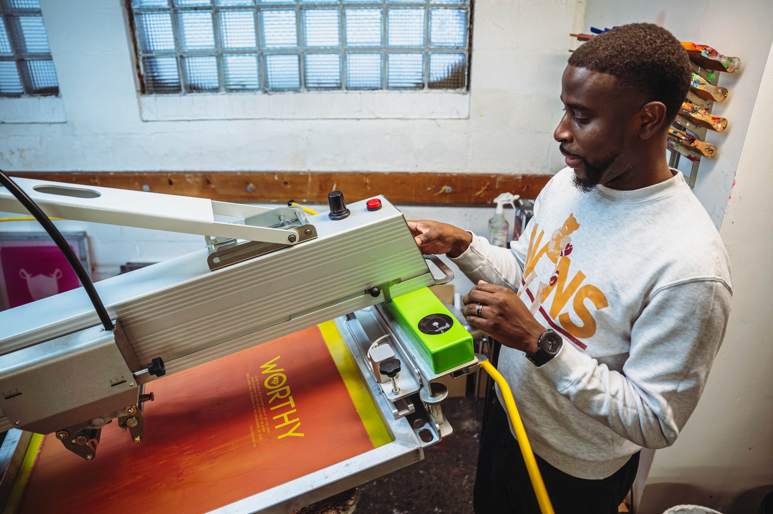 Man operating a machine printing a yellow word on a red surface in a workshop.
