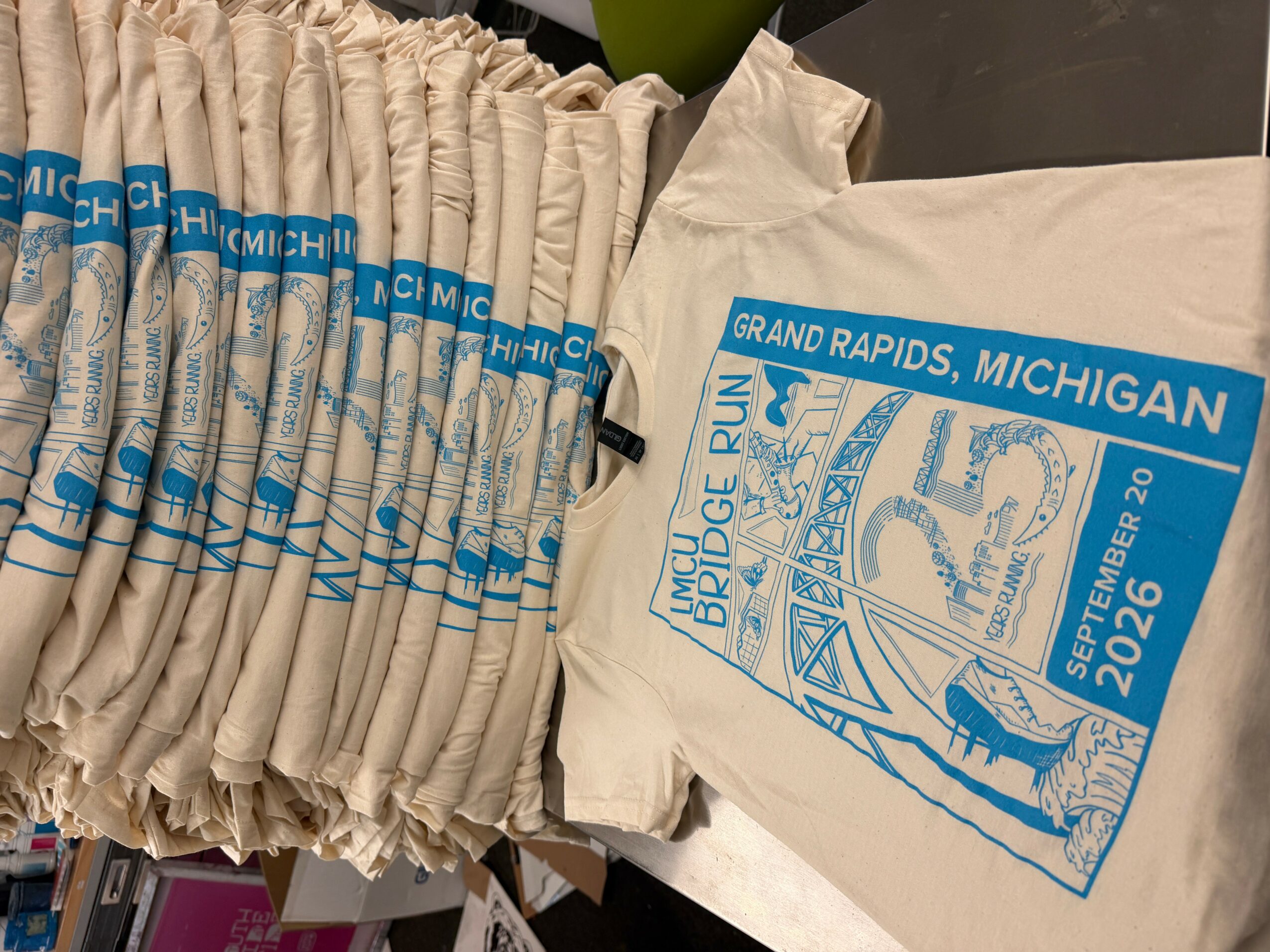 Tote bag with event logo and date, and a stack of event T-shirts, on a table.