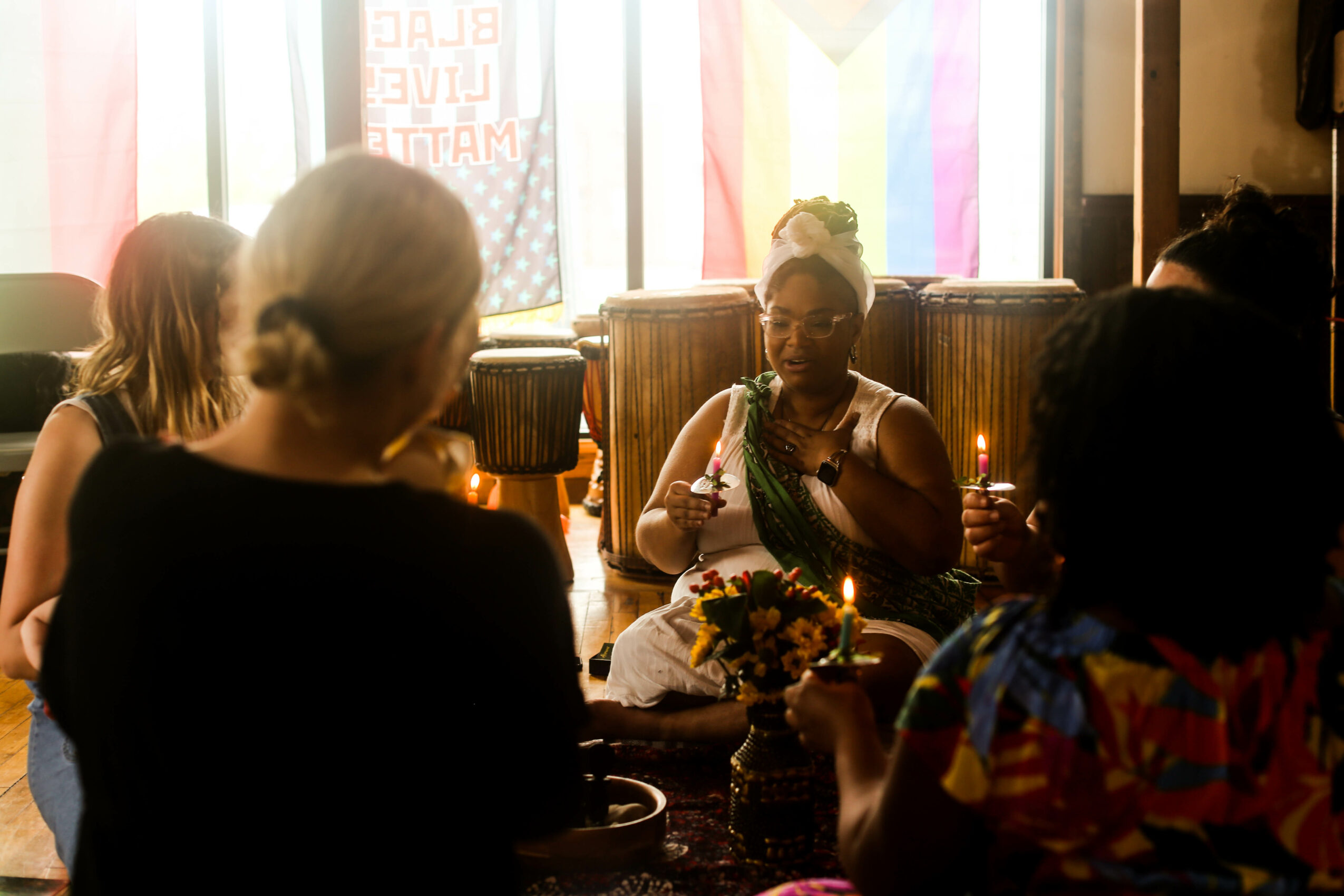 Group of women sitting at a table with drinks and flowers, sunlight streaming through colorful curtains behind them.