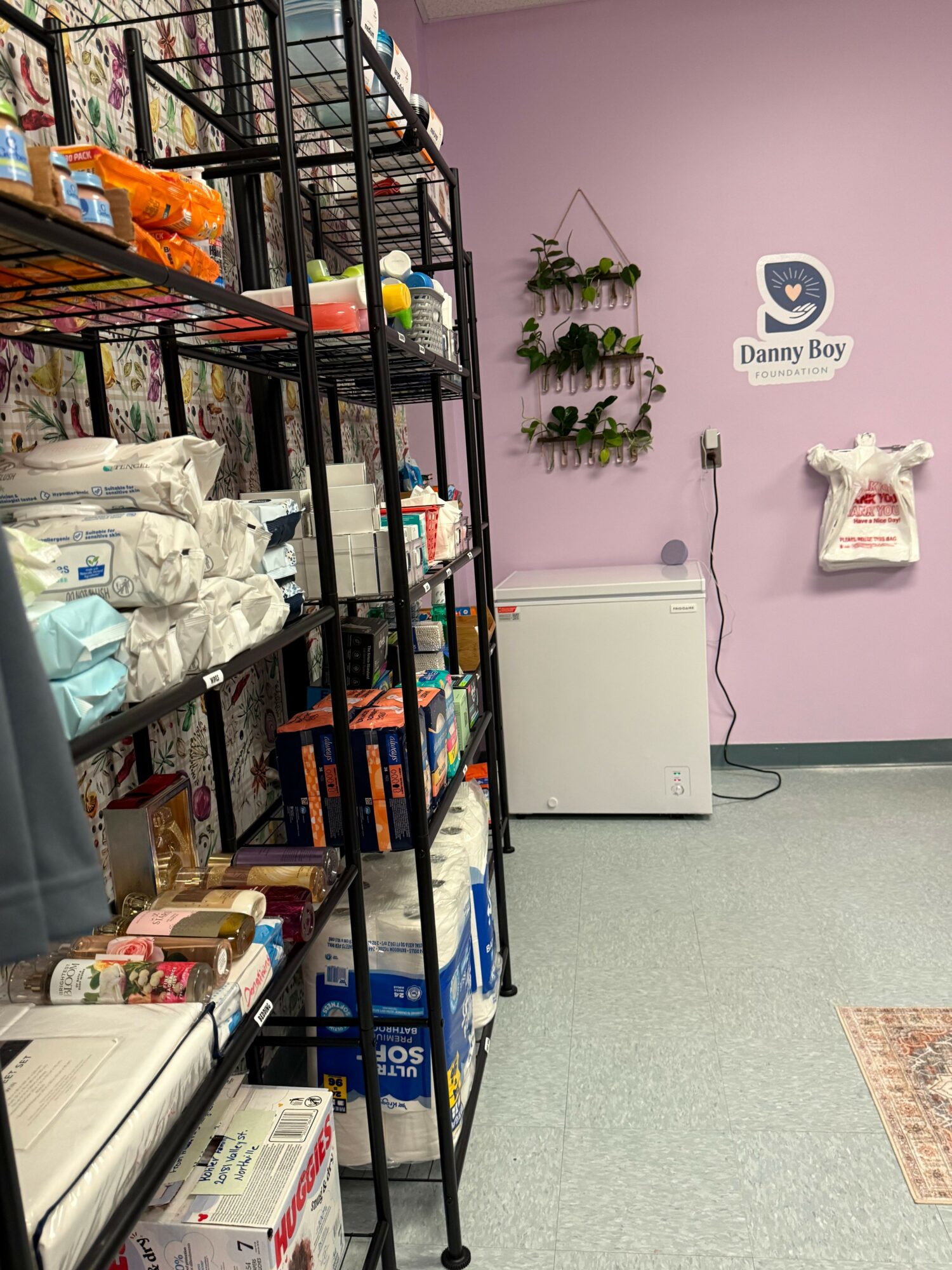 View of a store interior with shelves stocked with various products, a pink wall with a sign, and a white appliance.