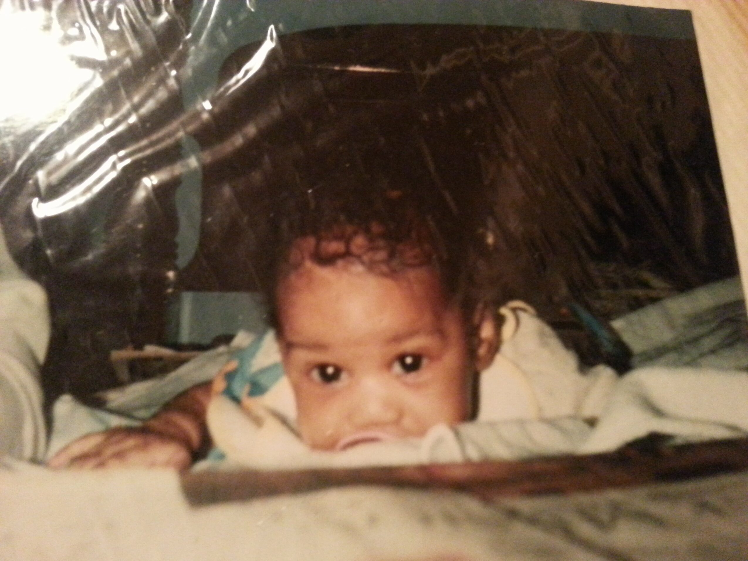 Child lying on bed with head resting on pillow, looking at camera, with dark background and bedding visible