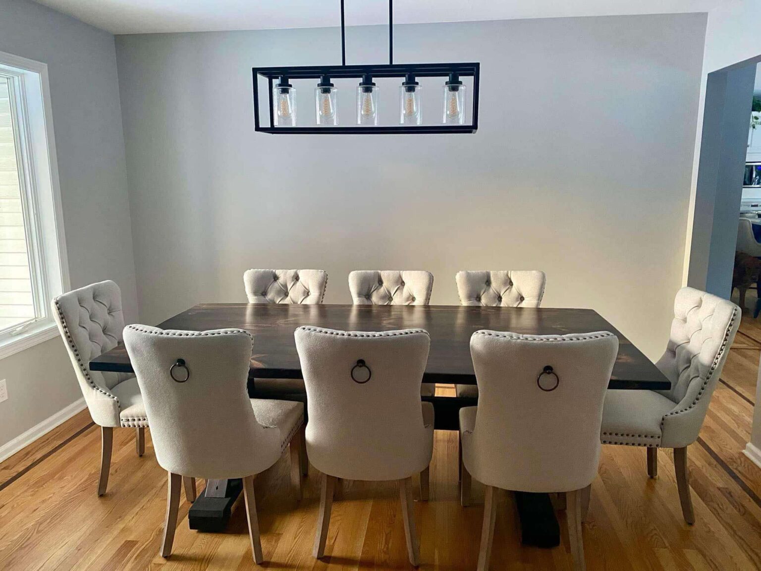 Dining room with a dark wooden table and eight upholstered chairs, a rectangular light fixture above, and a window on the left.