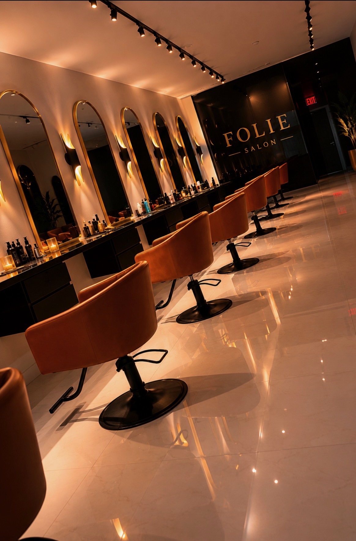 Salon with mirrors, chairs, and a black wall with gold lettering, illuminated by warm lighting.
