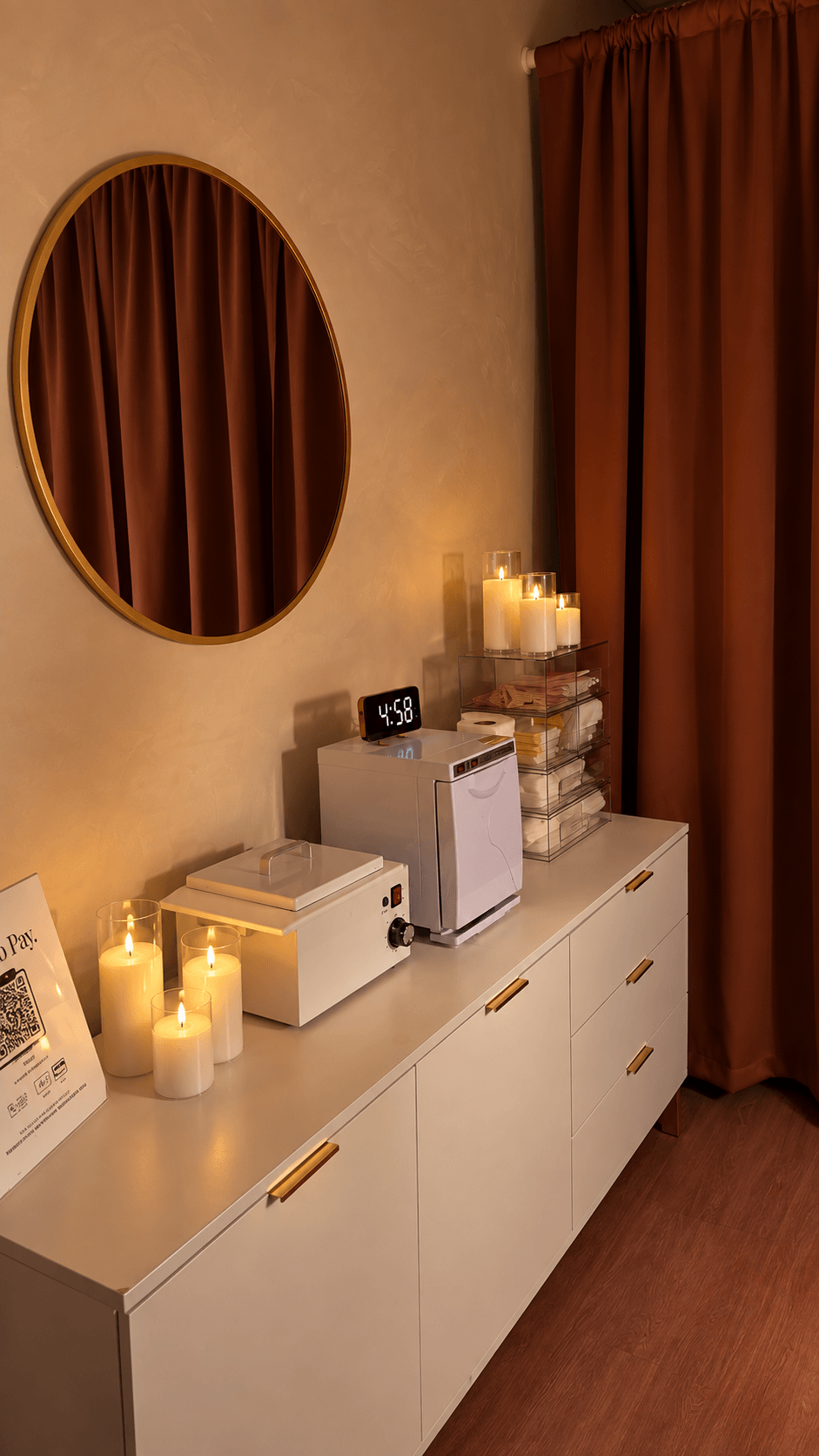 White cabinet with candles, a mirror, and decorative items against a beige wall with brown curtains.