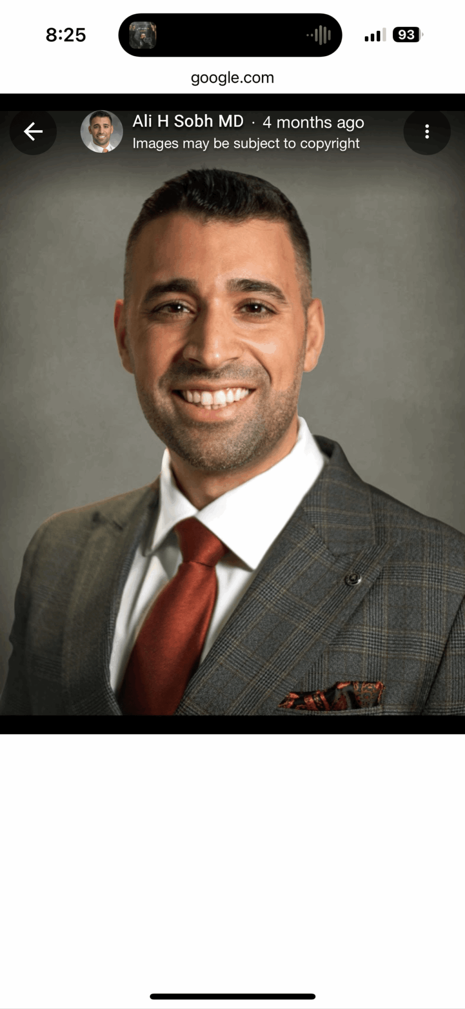 Man in suit smiling, gray background, wearing a white shirt and red tie.