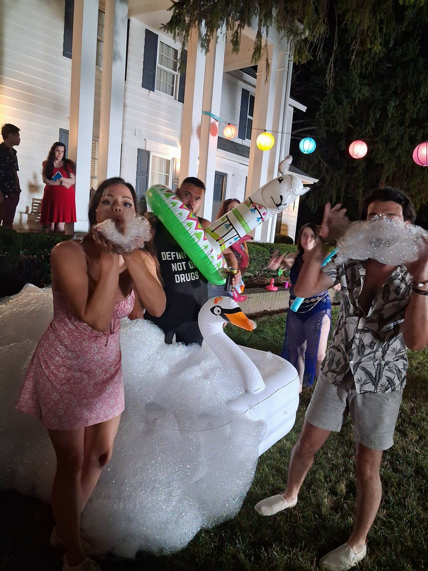 People playing in a pool with foam, inflatable float, and colorful balls outdoors, with a house in the background.