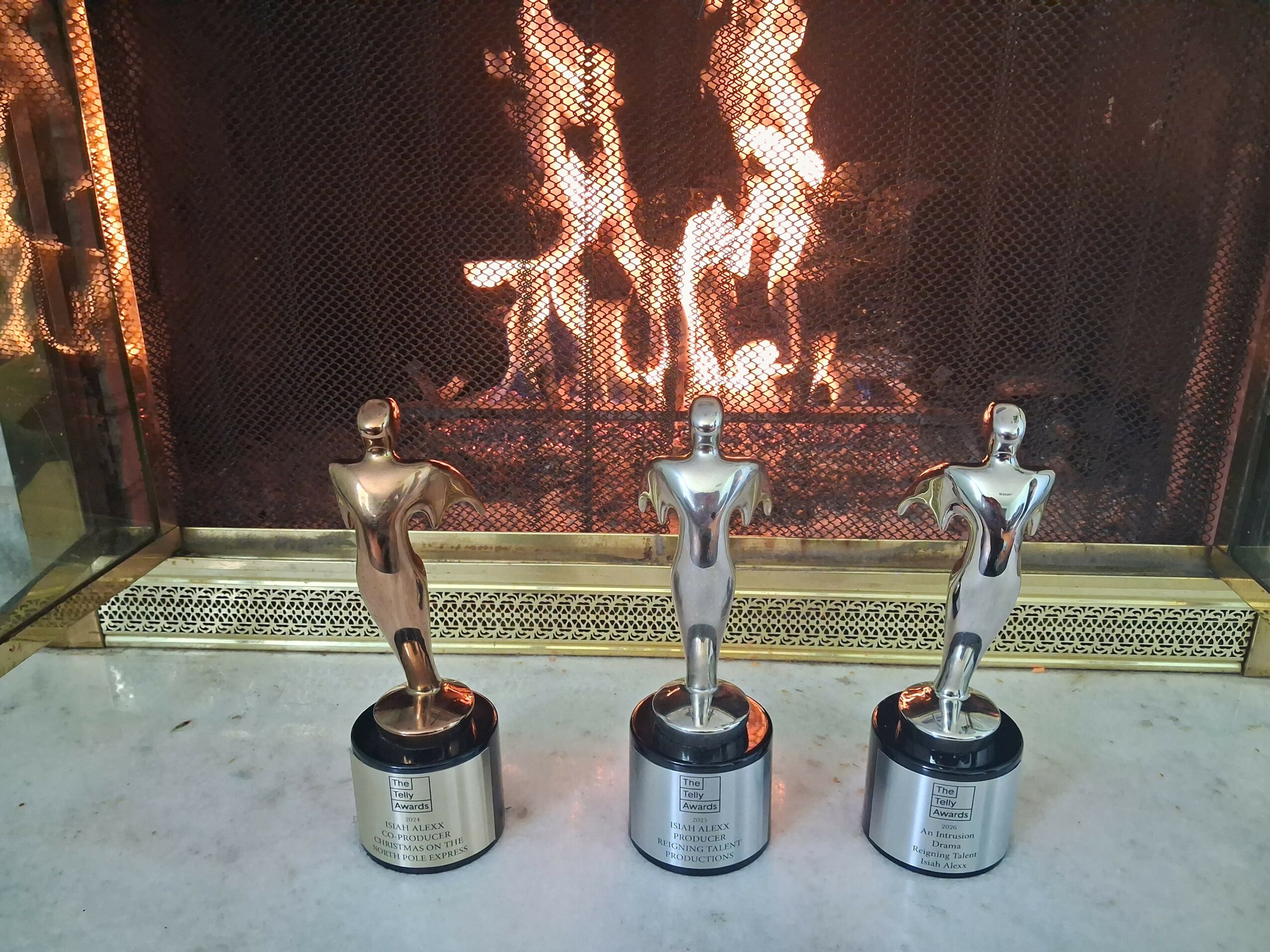 Three silver trophy statues with black bases in front of a fireplace with a fire burning inside.
