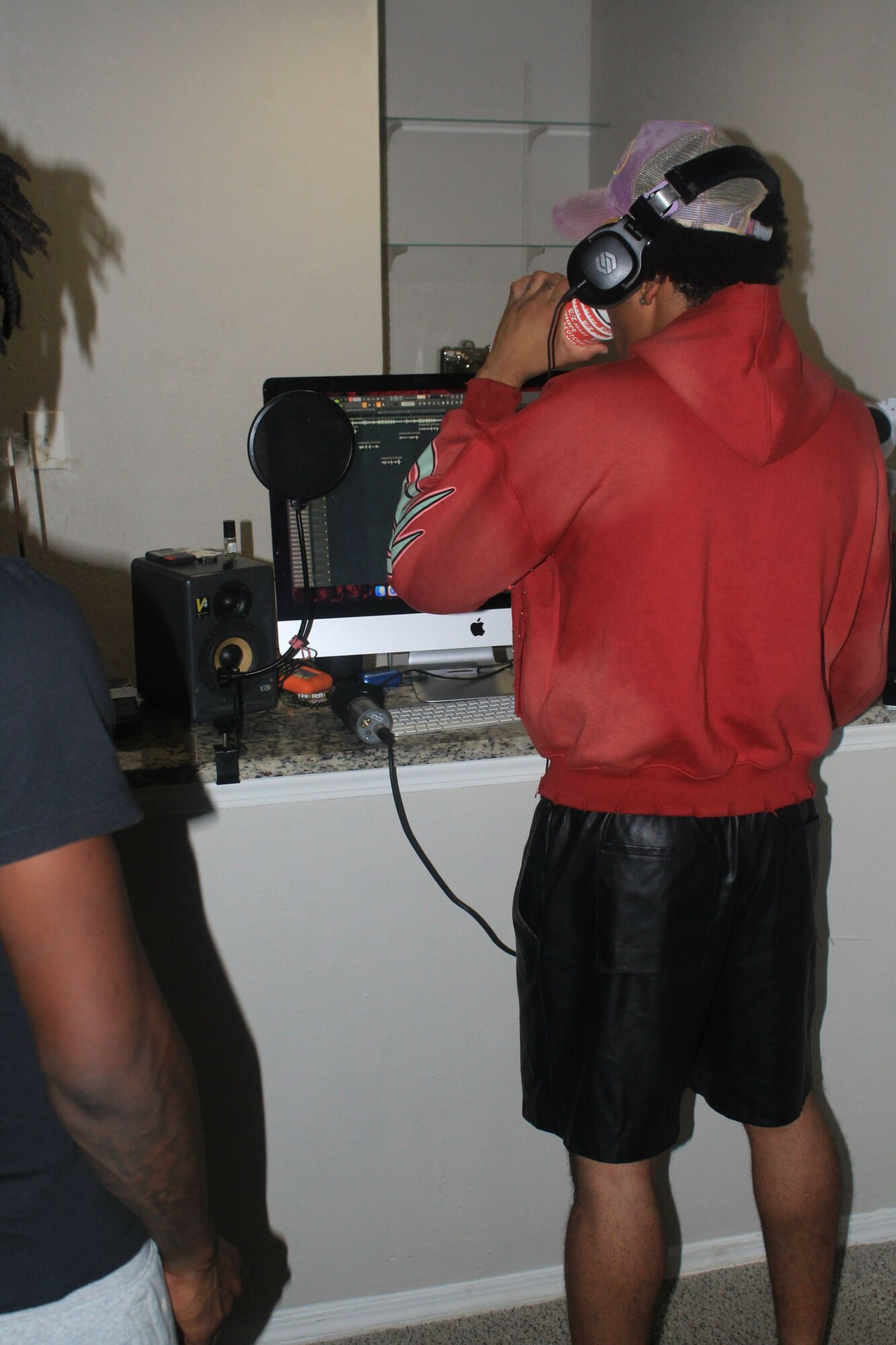 Person wearing a red shirt, black shorts, and a cap with headphones, standing in front of DJ equipment.
