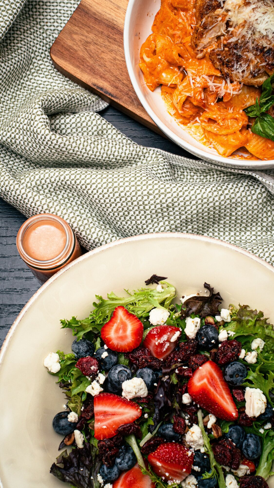Plate of mixed berry salad with strawberries, blueberries, and feta cheese, on a dark wooden table with a green cloth.