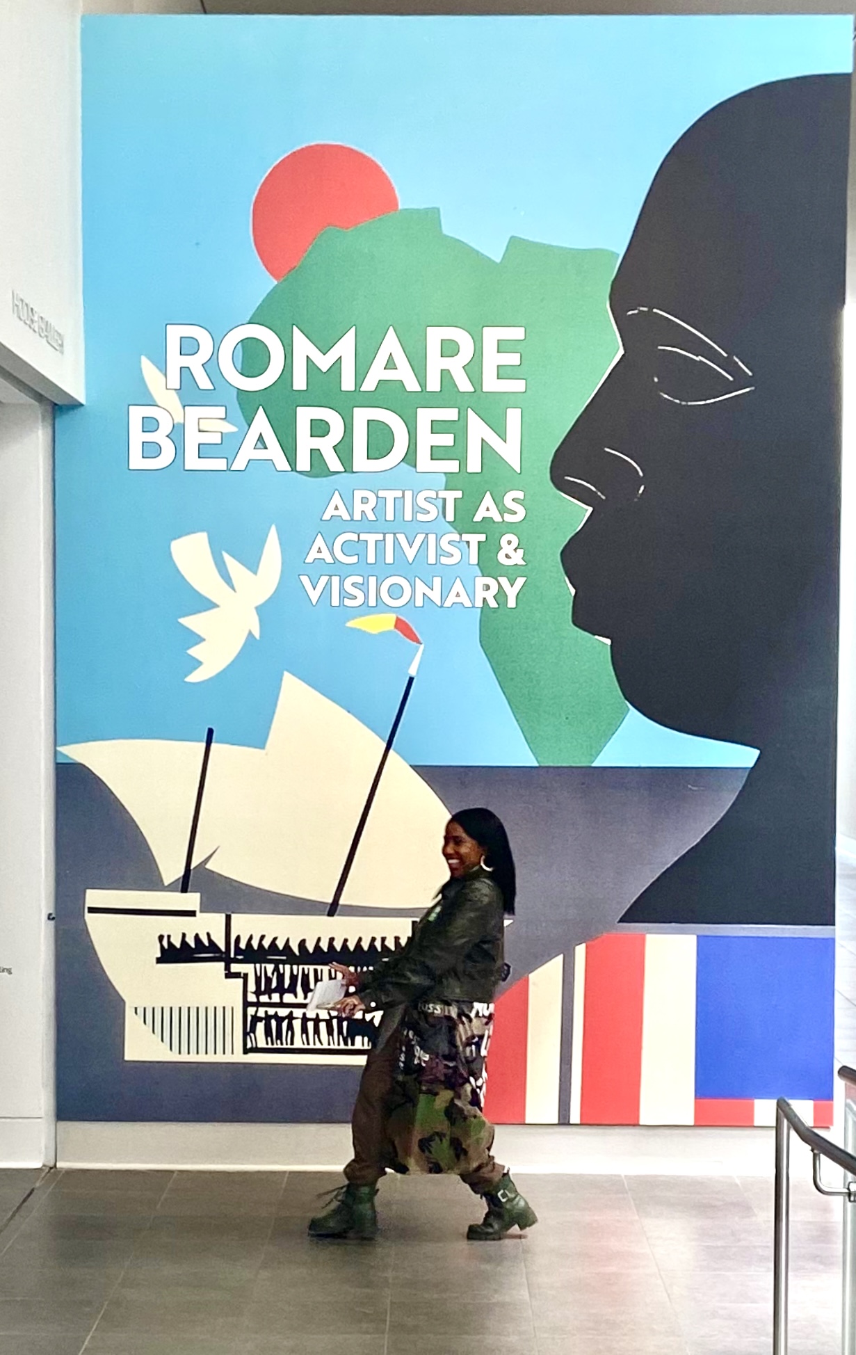 Person walking past a large mural of a woman's profile, a ship, and abstract shapes, with text about Romare Bearden.