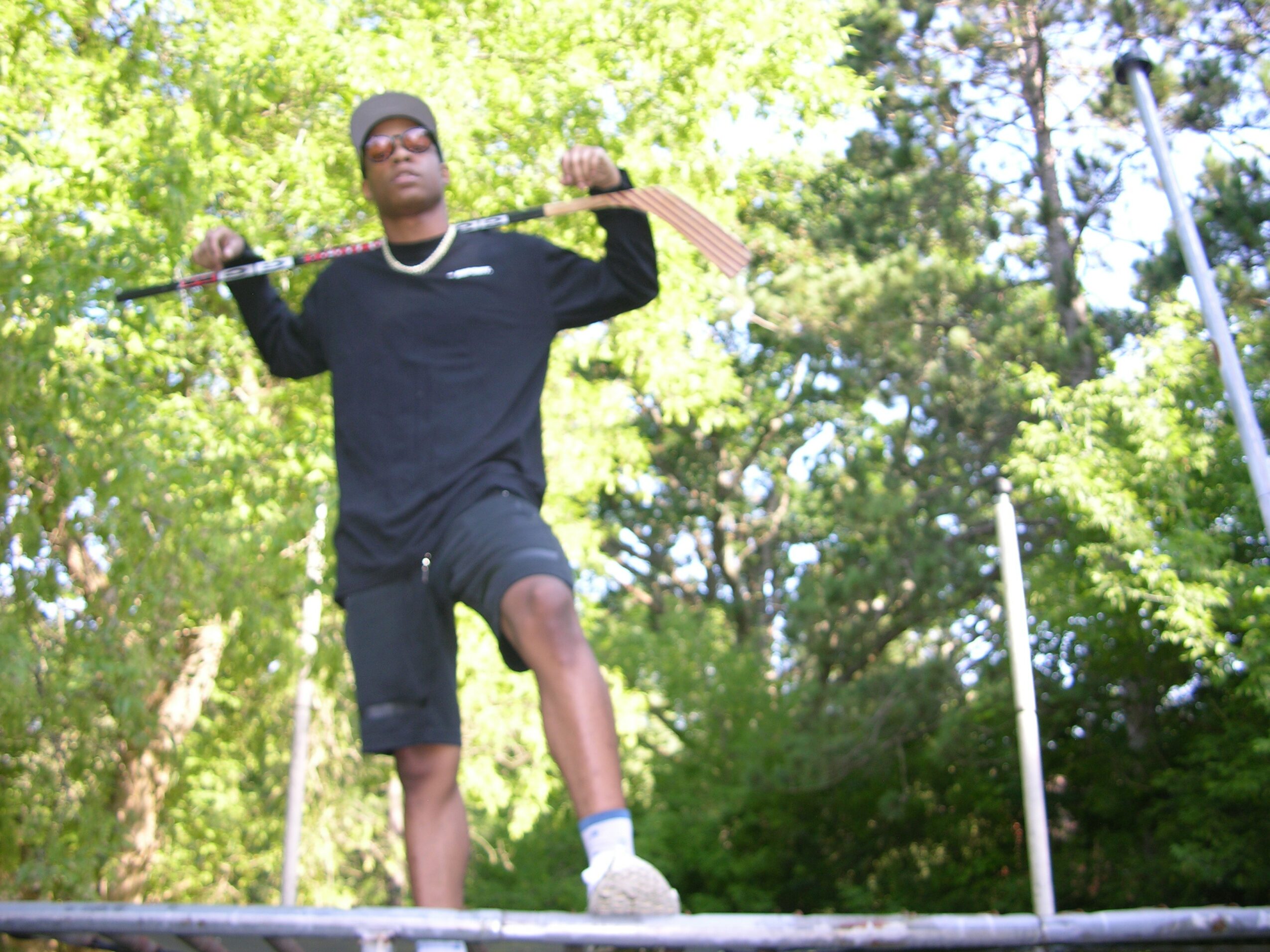 Young man lifting a barbell outdoors with trees in the background.