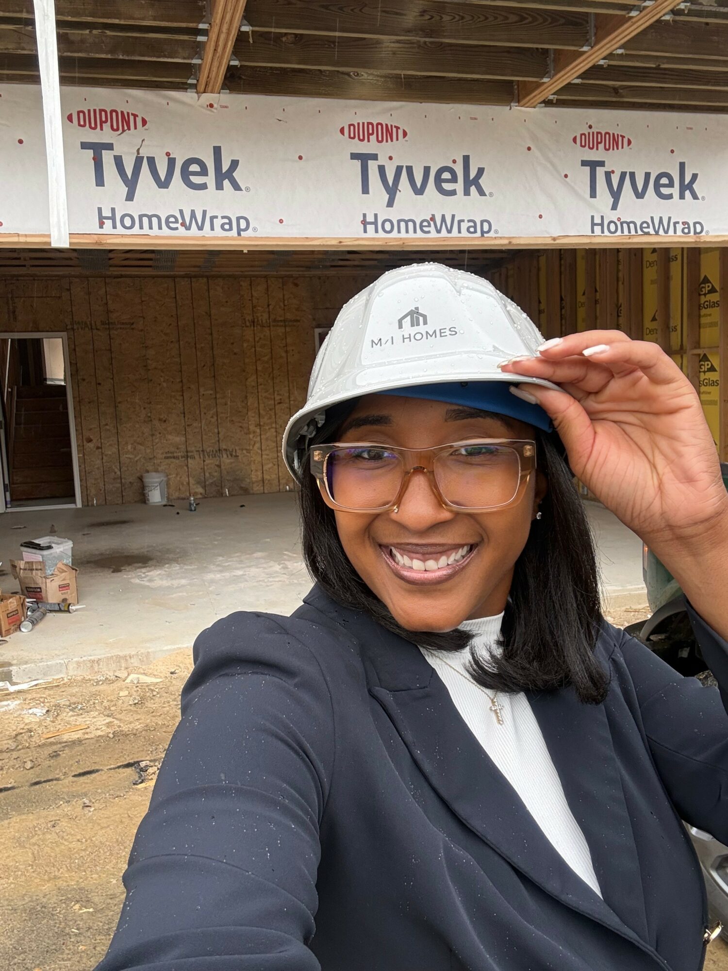 Woman in a suit and safety helmet smiling at construction site with Tyvek HomeWrap in background.