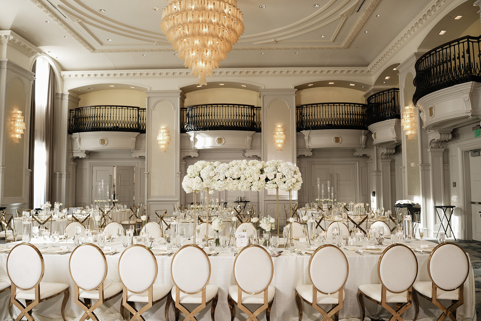 Elegant banquet hall with a large round table, floral centerpiece, chandelier, and ornate architecture.