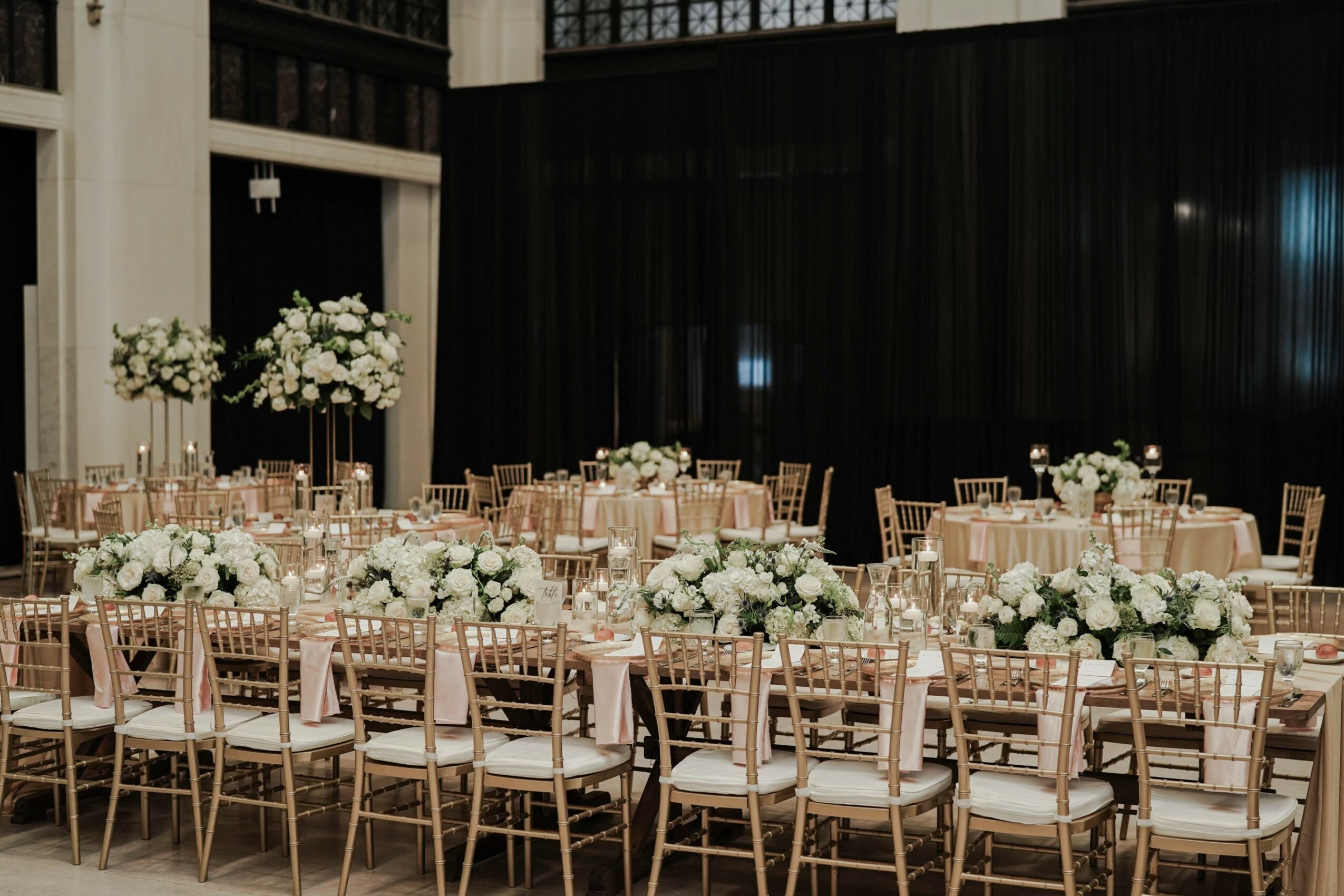 Elegant event space with tables decorated with white flowers and chairs, black curtains in the background.