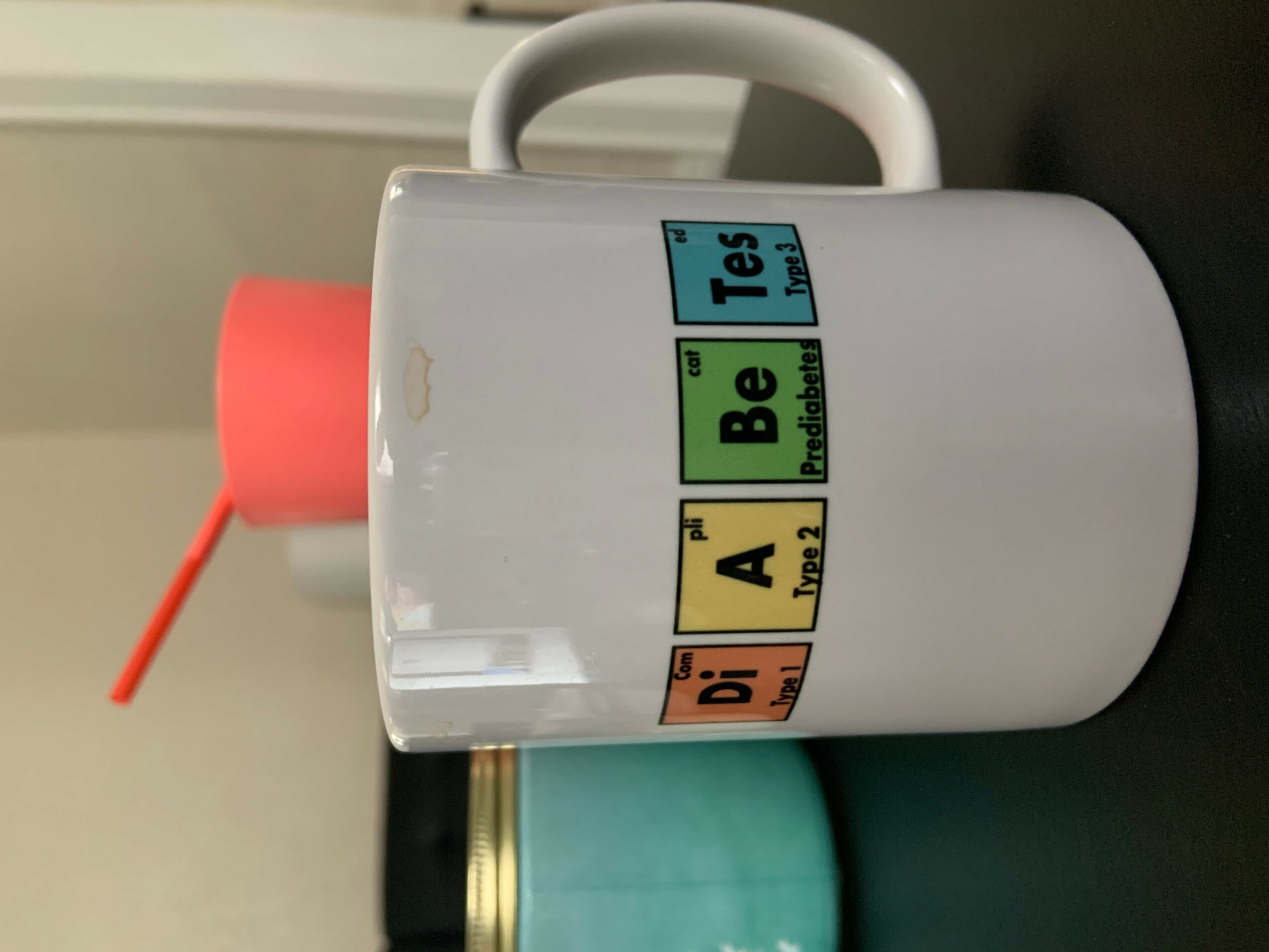 White mug with colorful text, handle at the top, and a red straw in the background.