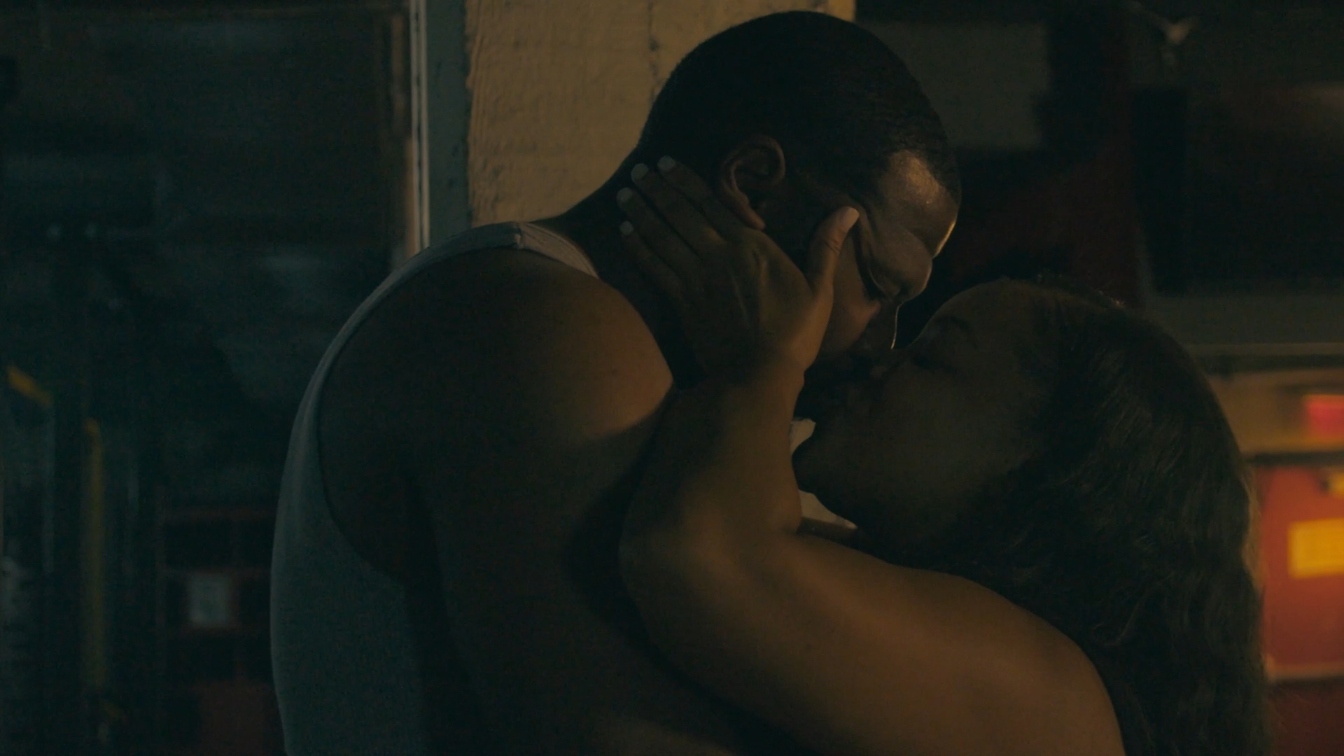Two people kissing in a dimly lit setting, one holding a phone to their ear.