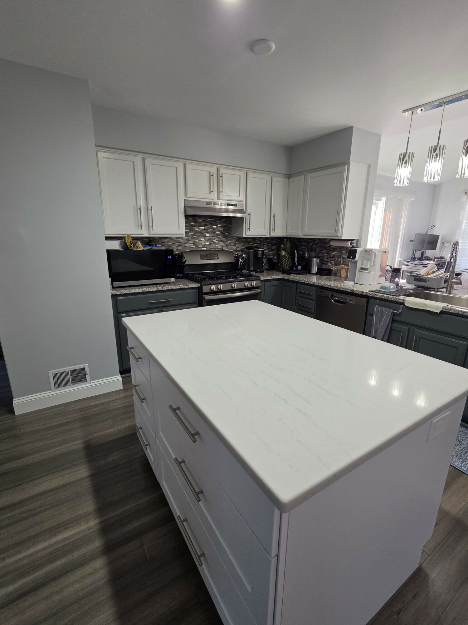 Kitchen with white cabinets, a large white island, and a dark countertop, viewed from the side.