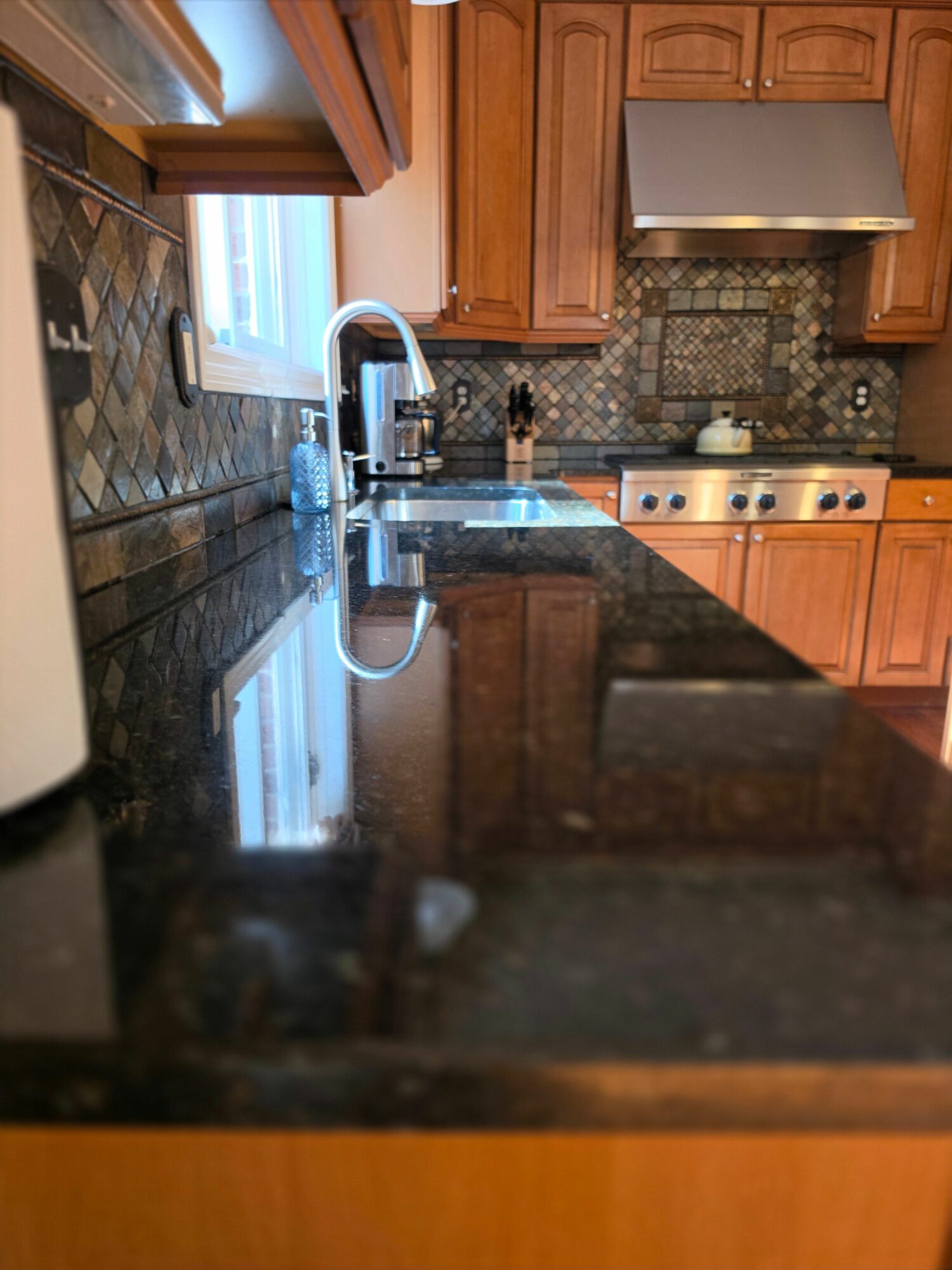 Kitchen with wooden cabinets, stove, and a black countertop, viewed from a tilted angle.