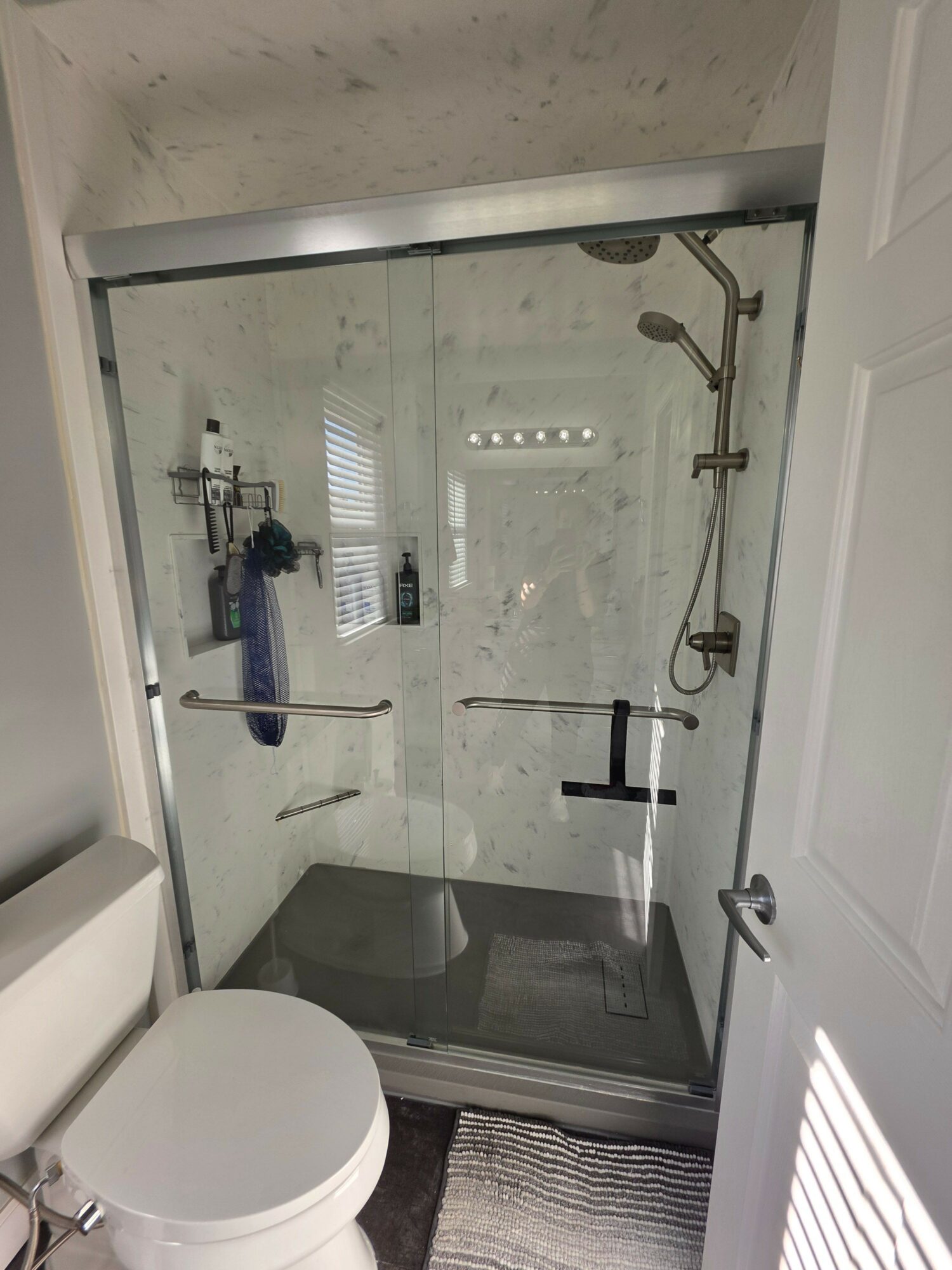 Bathroom shower with glass door, showerhead, and toiletries inside, viewed from outside the shower area.