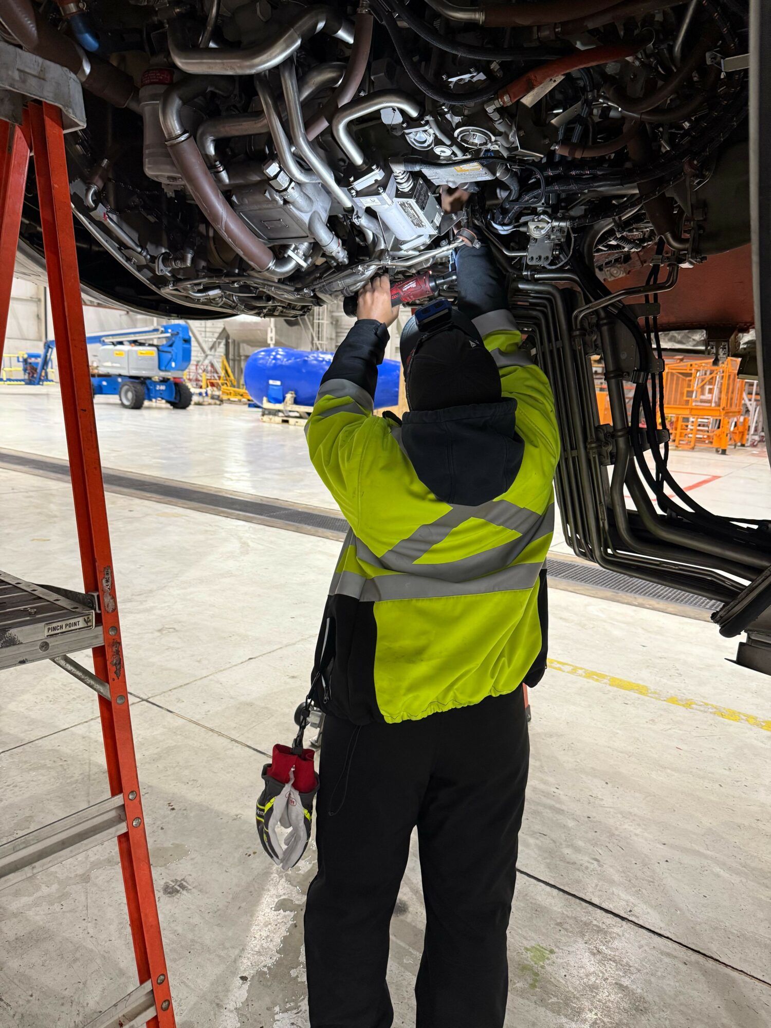Worker in high-visibility vest inspecting engine components in a garage or workshop.