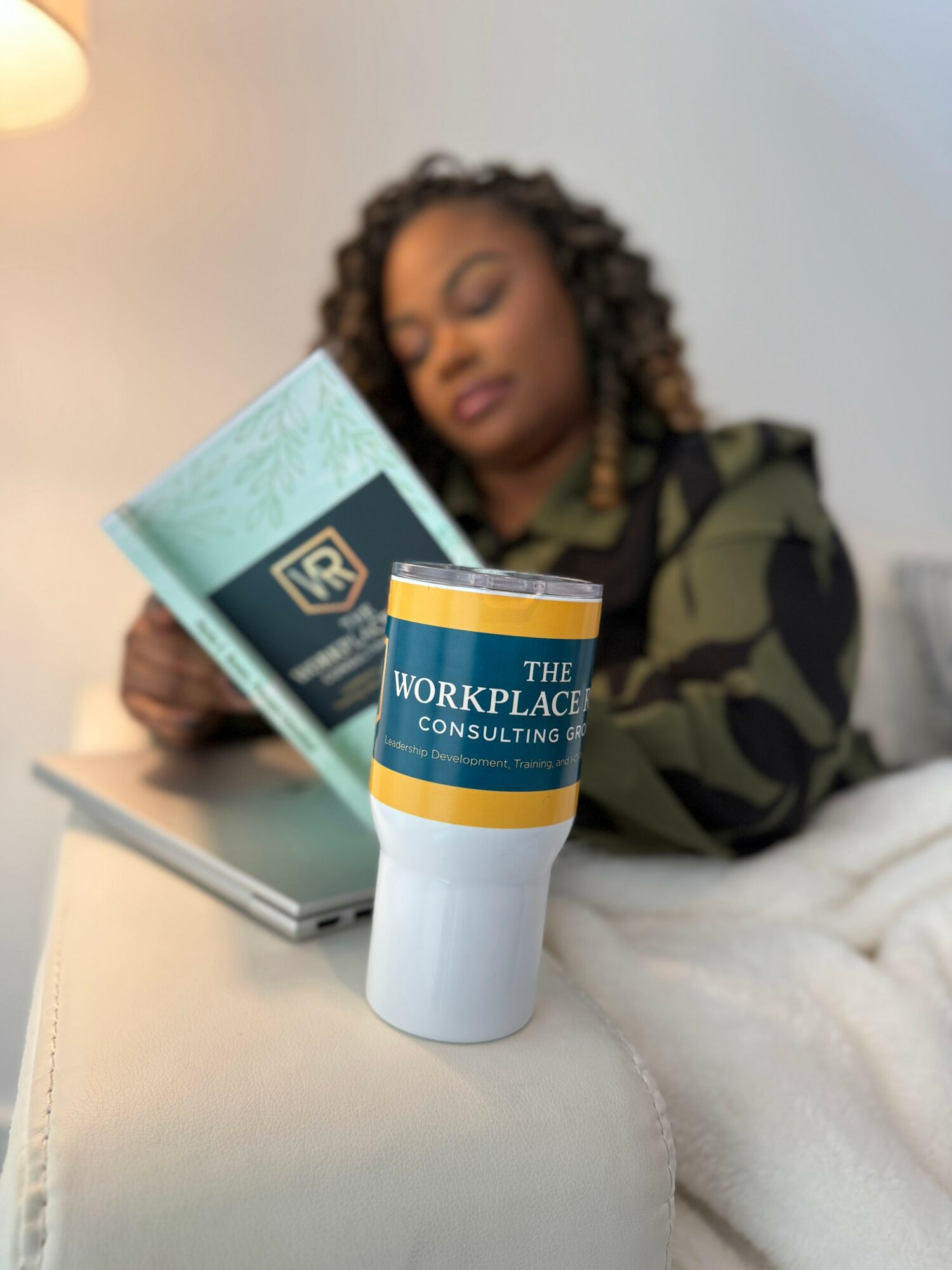Woman reading a book with a coffee cup on a table in front of her, blurred background.