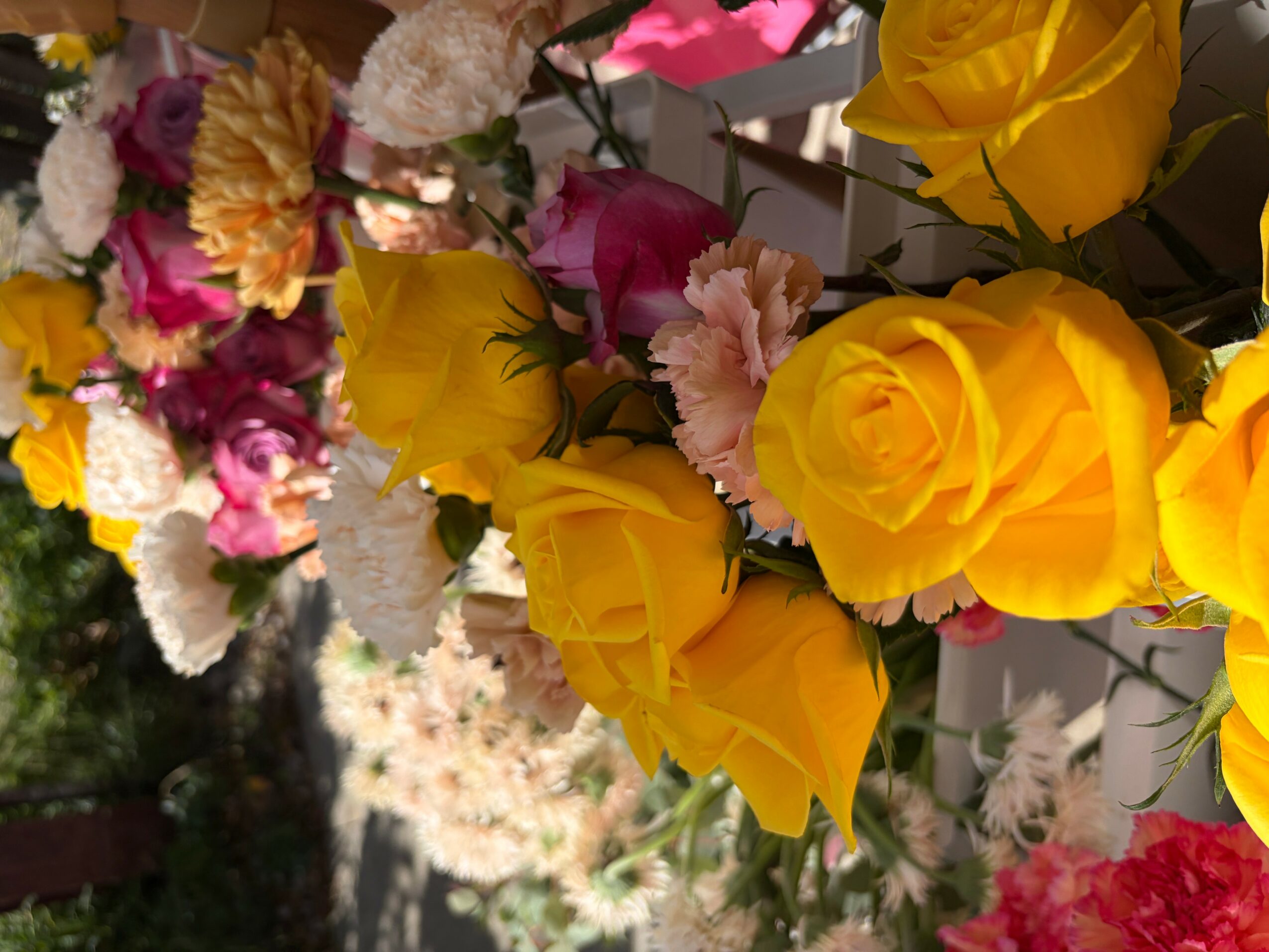 Close-up of yellow roses and pink, white, and purple flowers in a bouquet.