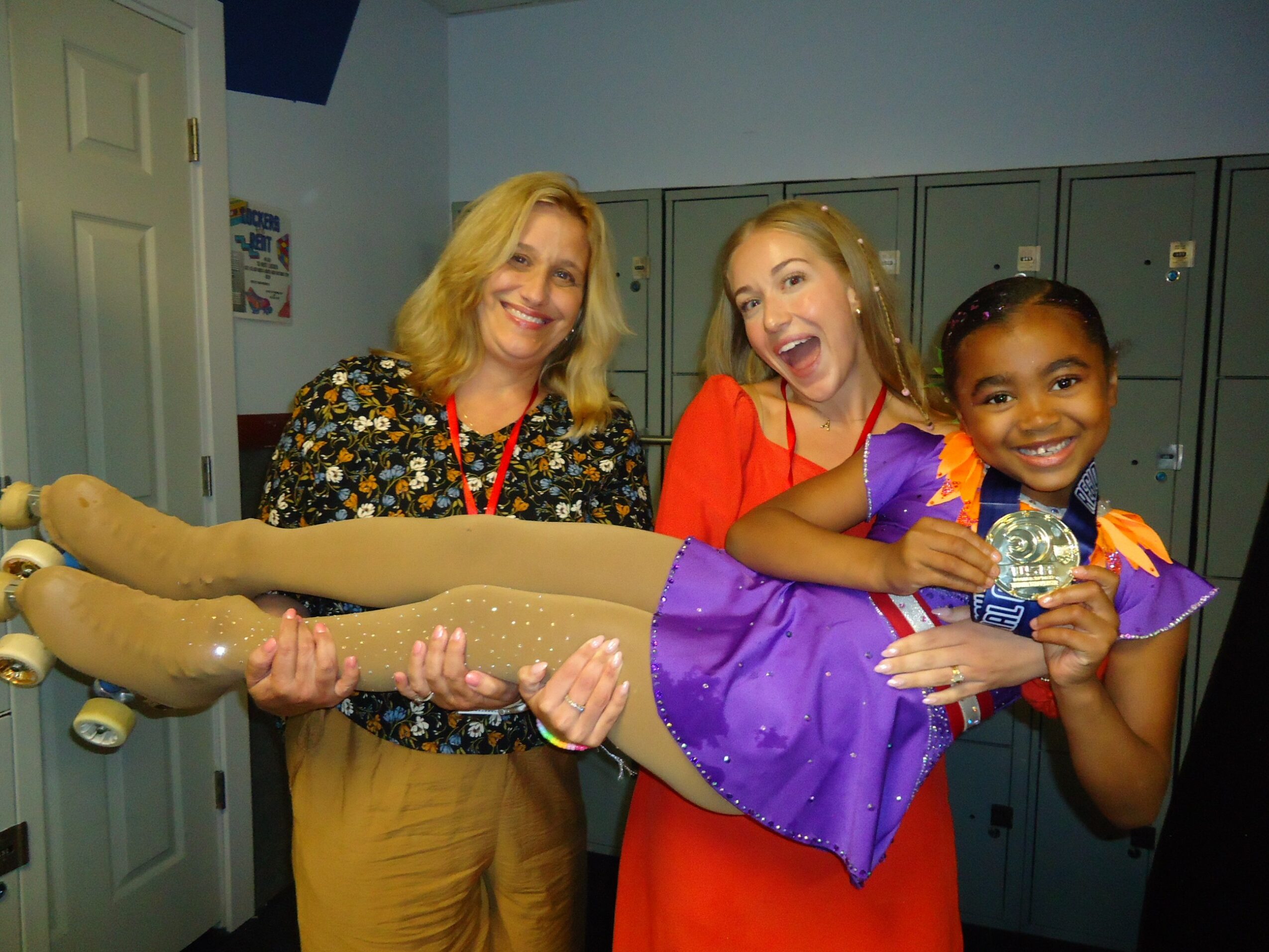 Three people, two women and a girl, smiling and holding a doll in a room with lockers.