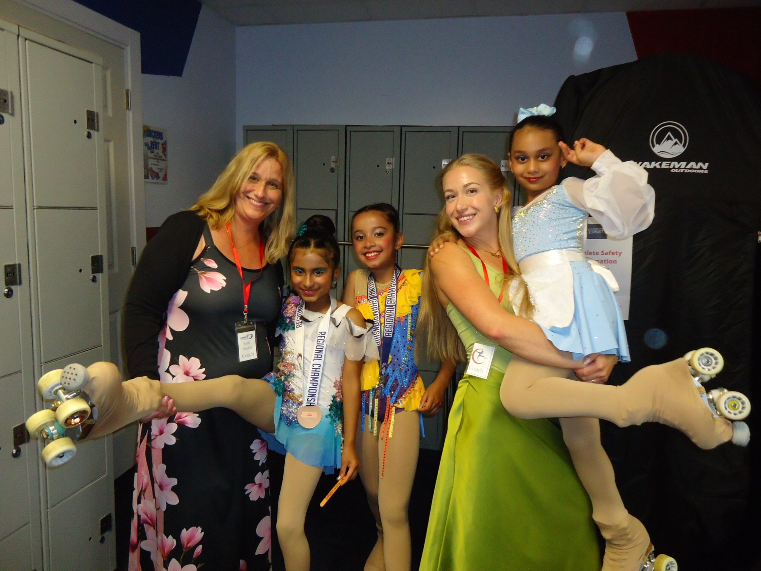 Group of five people, four girls and one woman, smiling and posing with roller skates in an indoor setting.