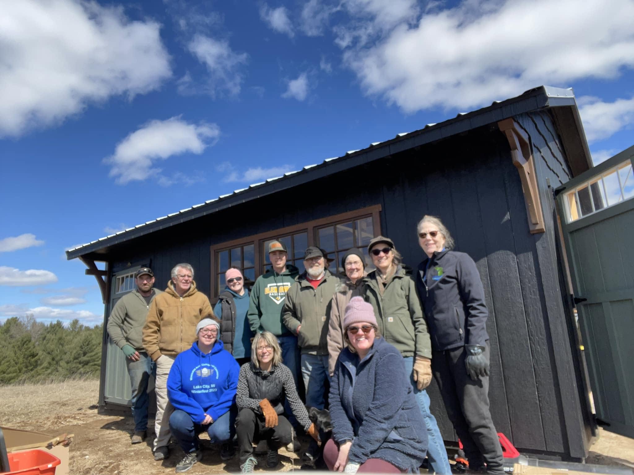 Group of ten people outdoors near a dark blue building with a cloudy sky background.