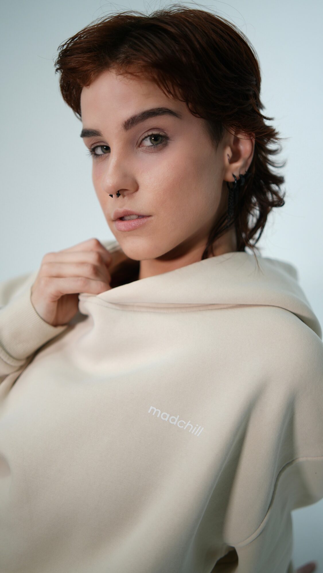 Young woman with short brown hair and light makeup, wearing a cream hoodie, looking at the camera.