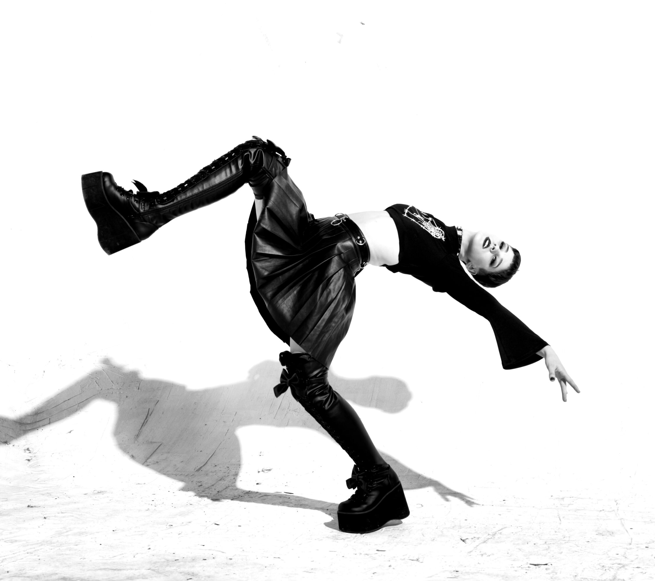 Person performing a dance move, balancing on one hand with legs extended, in black clothing against a white background.