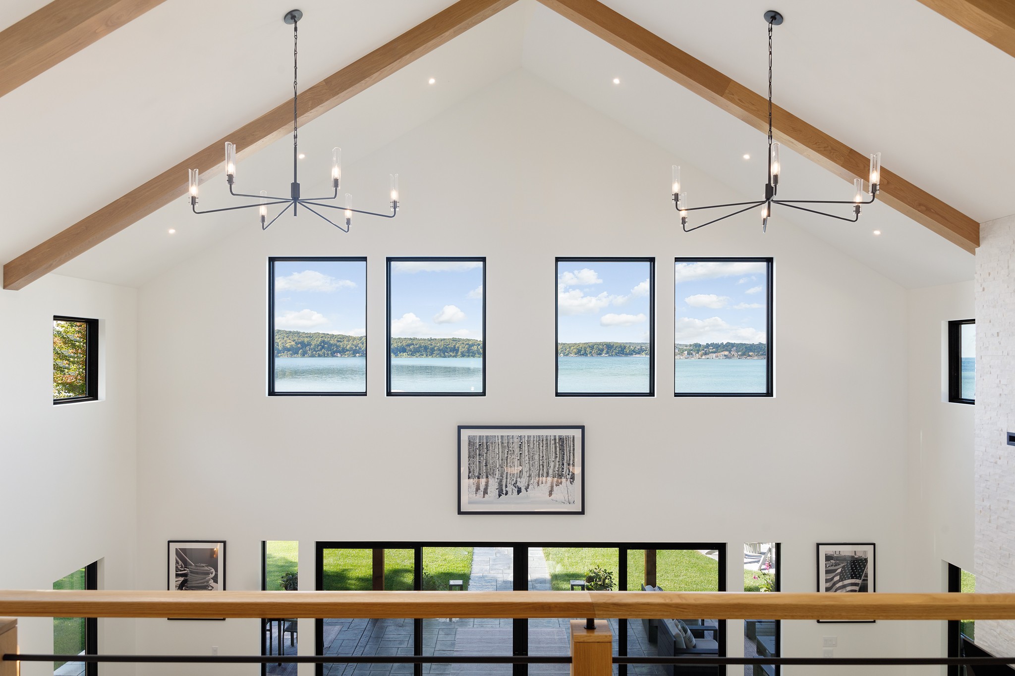 Interior view of a room with a high, sloped ceiling, four large windows, and two chandeliers, with a dining table and artwork.