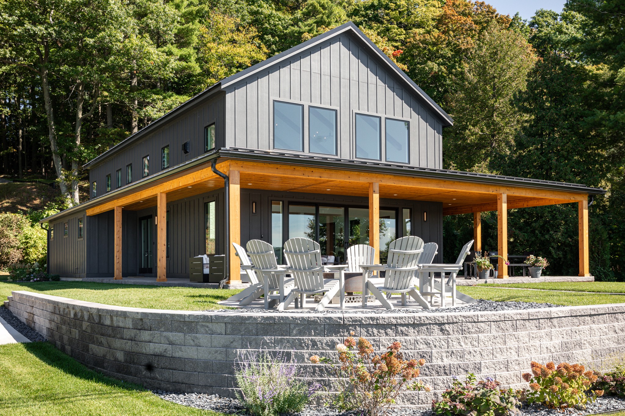Modern two-story house with a large covered patio, outdoor dining table, surrounded by trees and greenery.