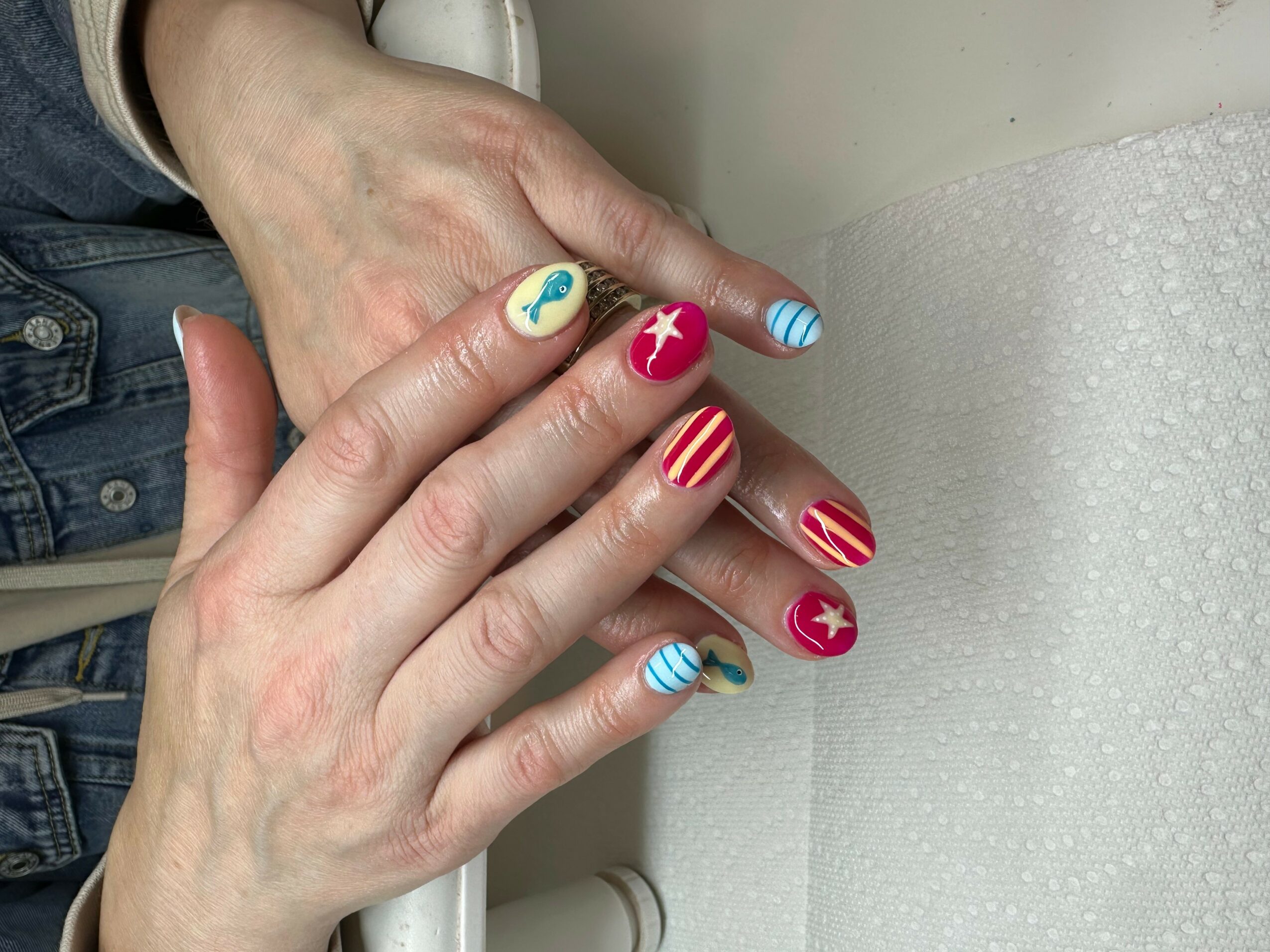 Hands with decorated nails resting on a white surface, nails painted with patriotic and nautical designs.