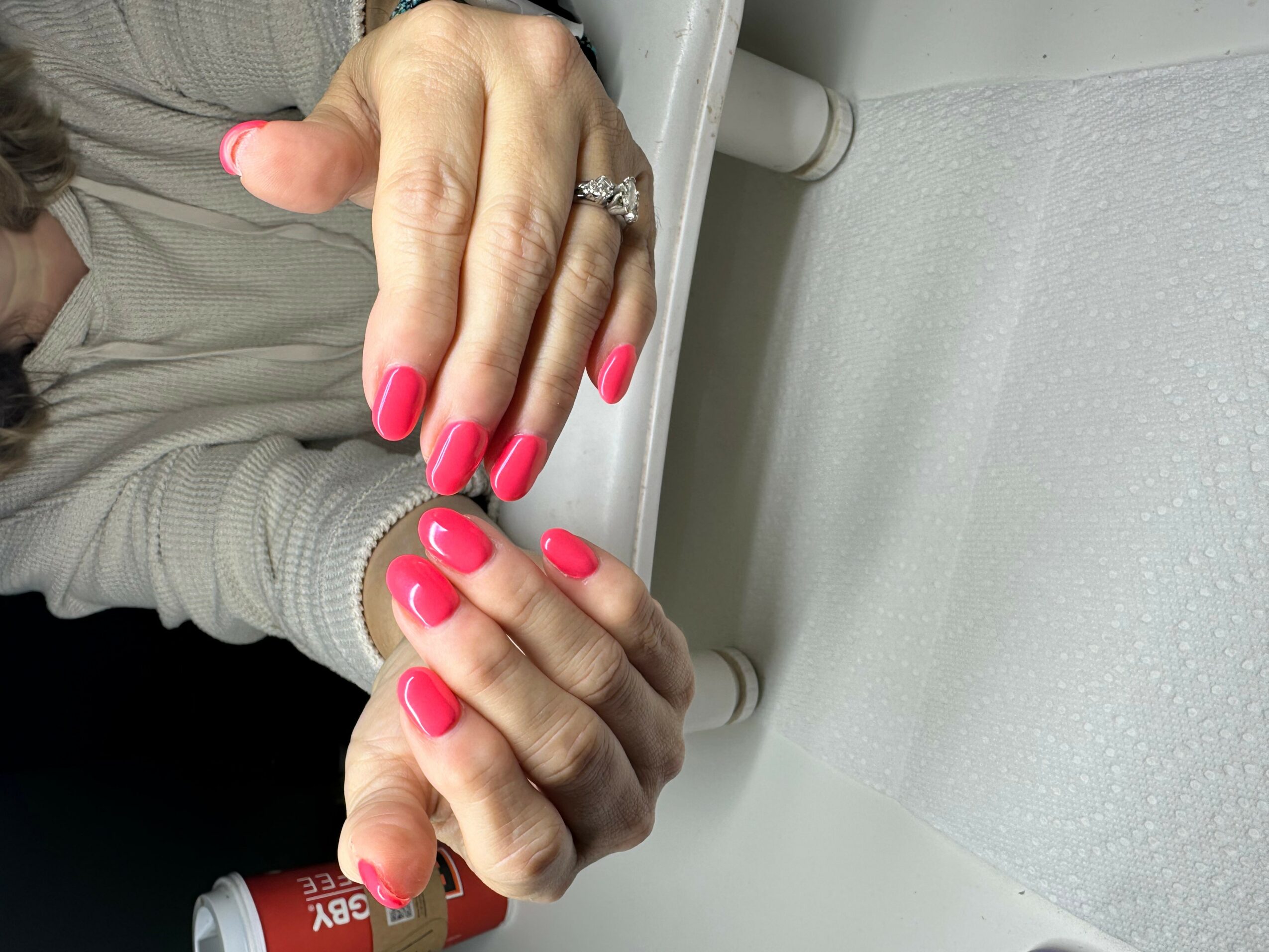 Close-up of hands with pink nail polish, one hand holding the other, on a white surface.