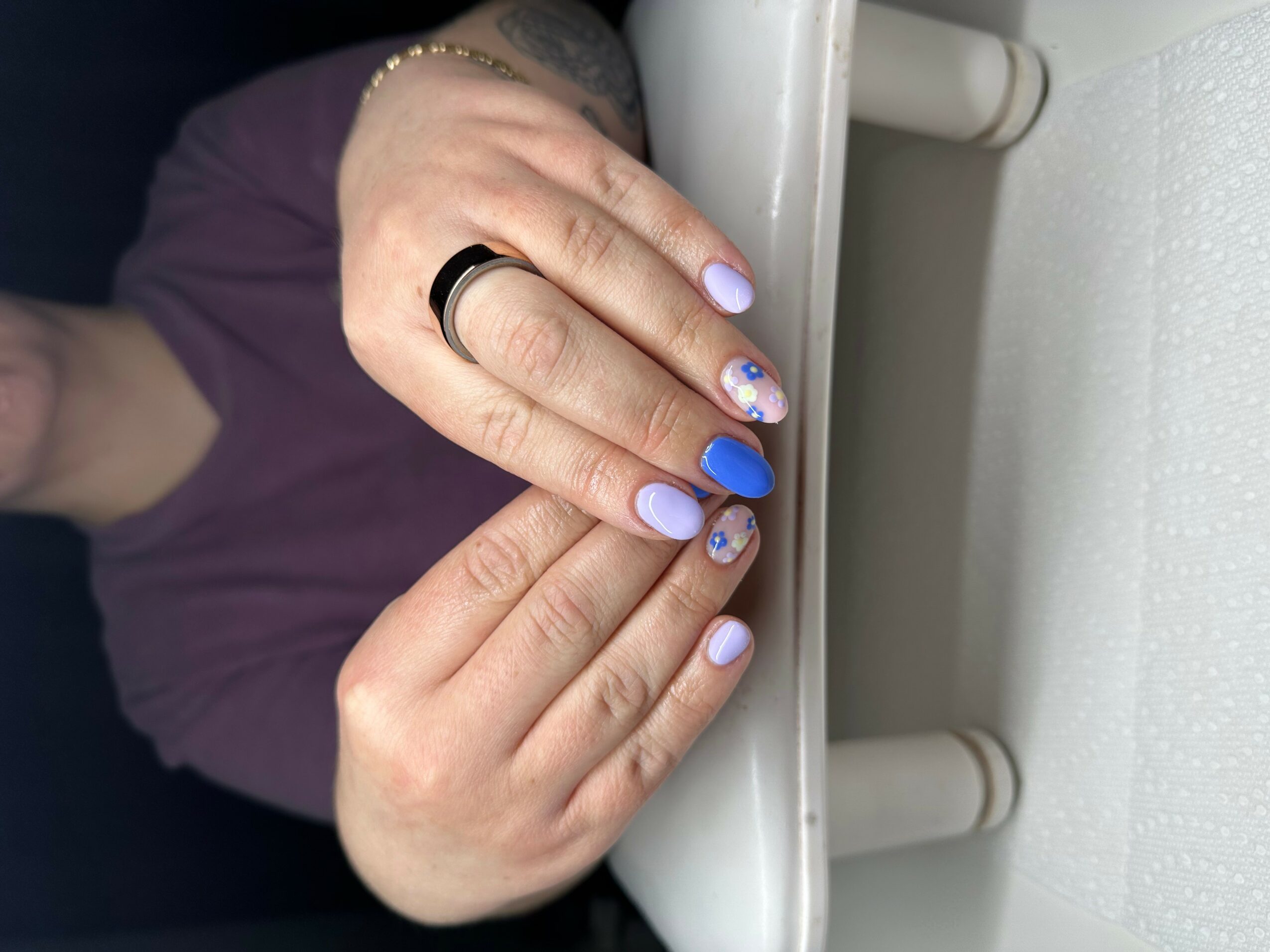 Person's hands resting on a white surface, showing nails painted in blue and decorated with small designs.
