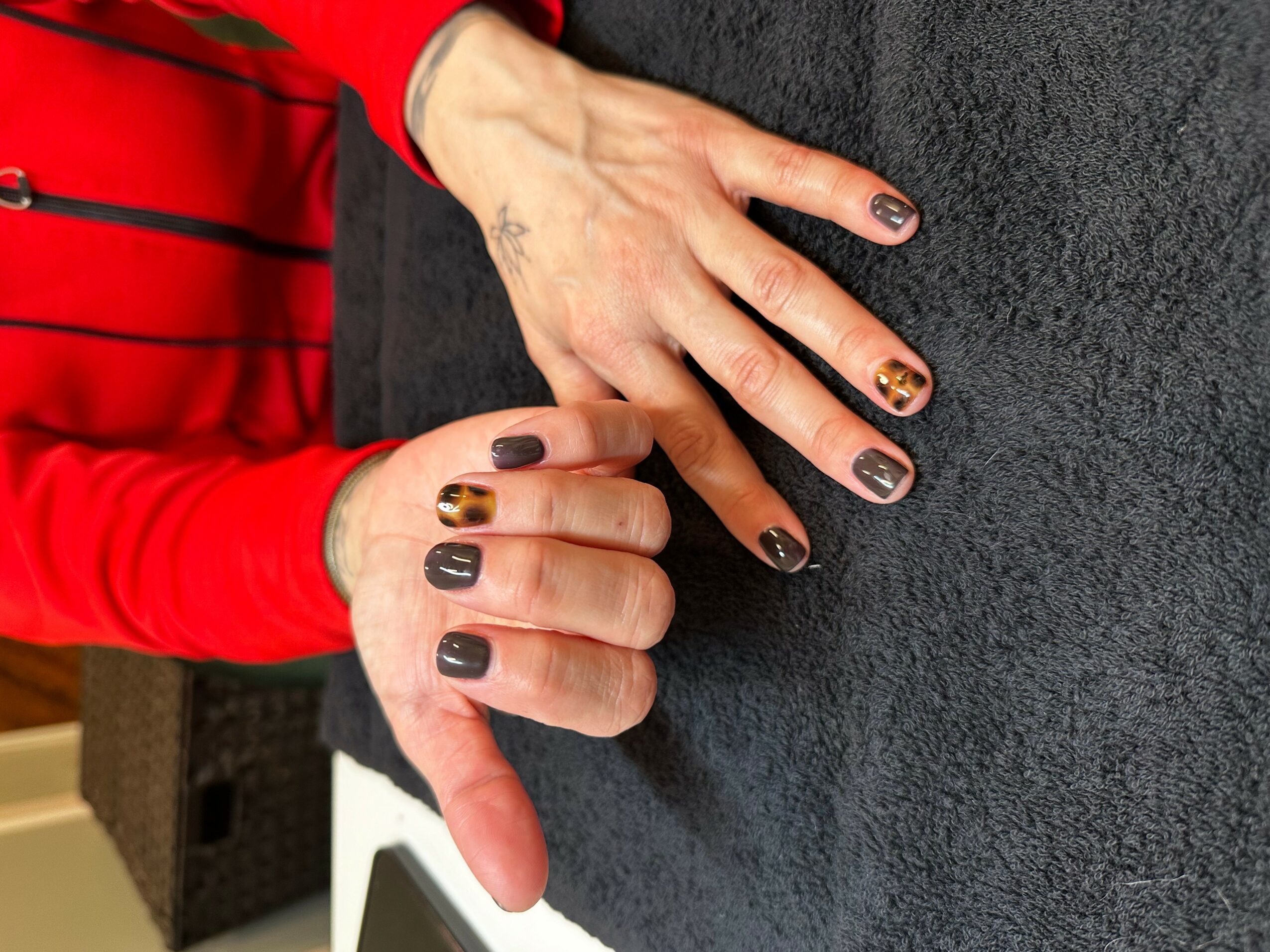 Hands with decorated nails resting on a dark surface, one hand giving a thumbs-up gesture, person wearing a red long-sleeve shirt.
