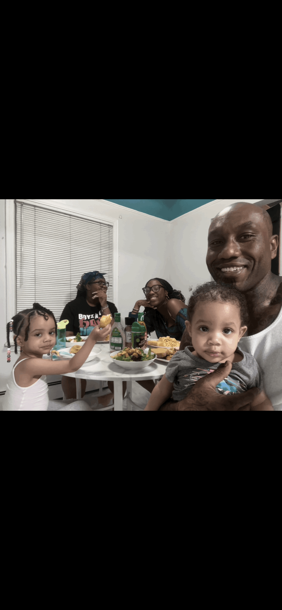 Family gathered around a table with food, smiling and enjoying a meal together indoors.