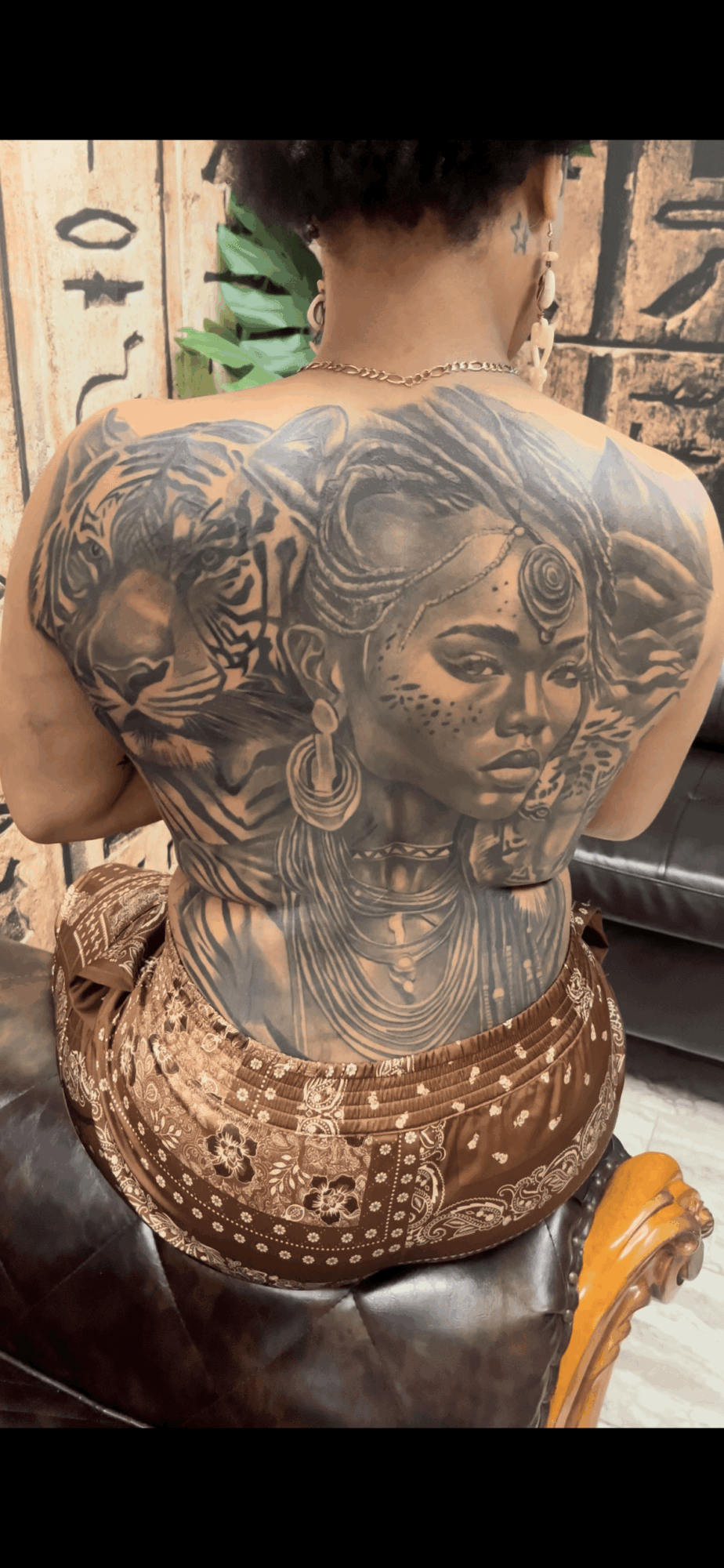 Back view of a person with a large, detailed tattoo of a woman's face and other intricate designs on their back.