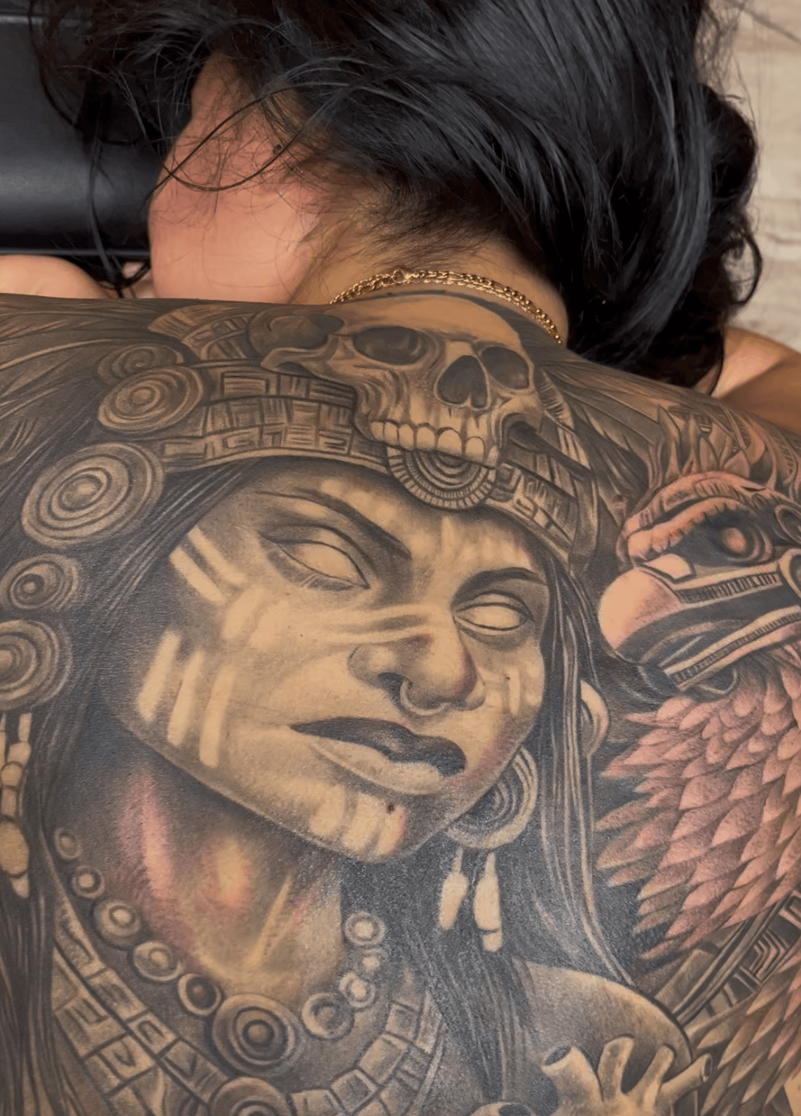 Close-up of a person's face with a large, detailed tattoo covering the shoulder and chest area, featuring a skull and tribal patterns.